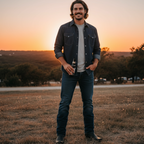 Man in jeans wearing The Shoal Creek boots, standing in a field at sunset