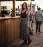 Woman in a floral maxi skirt holds a drink at an outdoor bar in cognac Trinity boots
