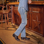 Man leans on a star-carved bar in jeans and The 6th Street brown python boots.