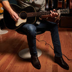 Man plays acoustic guitar seated, wearing The 6th Street brown python boots.