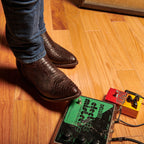 Man's feet on a wood floor beside guitar pedals in The 6th Street brown boots.