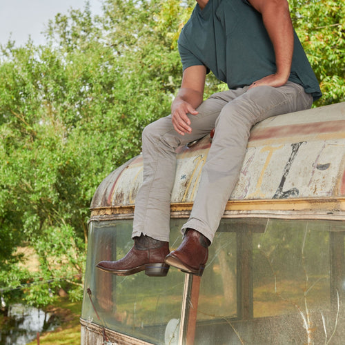 Man seated on a vintage bus roof wearing The Congress boots in brown lizard with jeans.