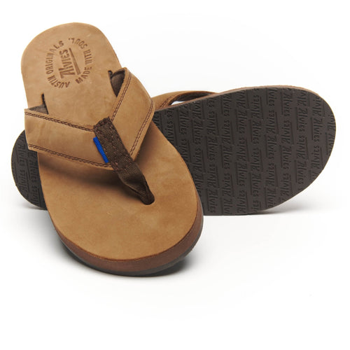 Woman's bare feet in tan Riverside flip-flops resting on a striped blanket poolside.